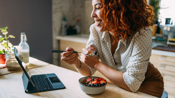 Mulher se alimenta com frutas em frente ao notebook para artigo de autocuidado na menopausa