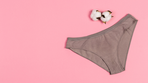 Calcinha nude sobre fundo rosa, com duas bolas de algodão in natura compondo o cenário.
