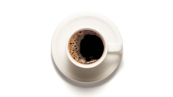 Xícara branca com café dentro, sobre um pires branco, em uma mesa branca.